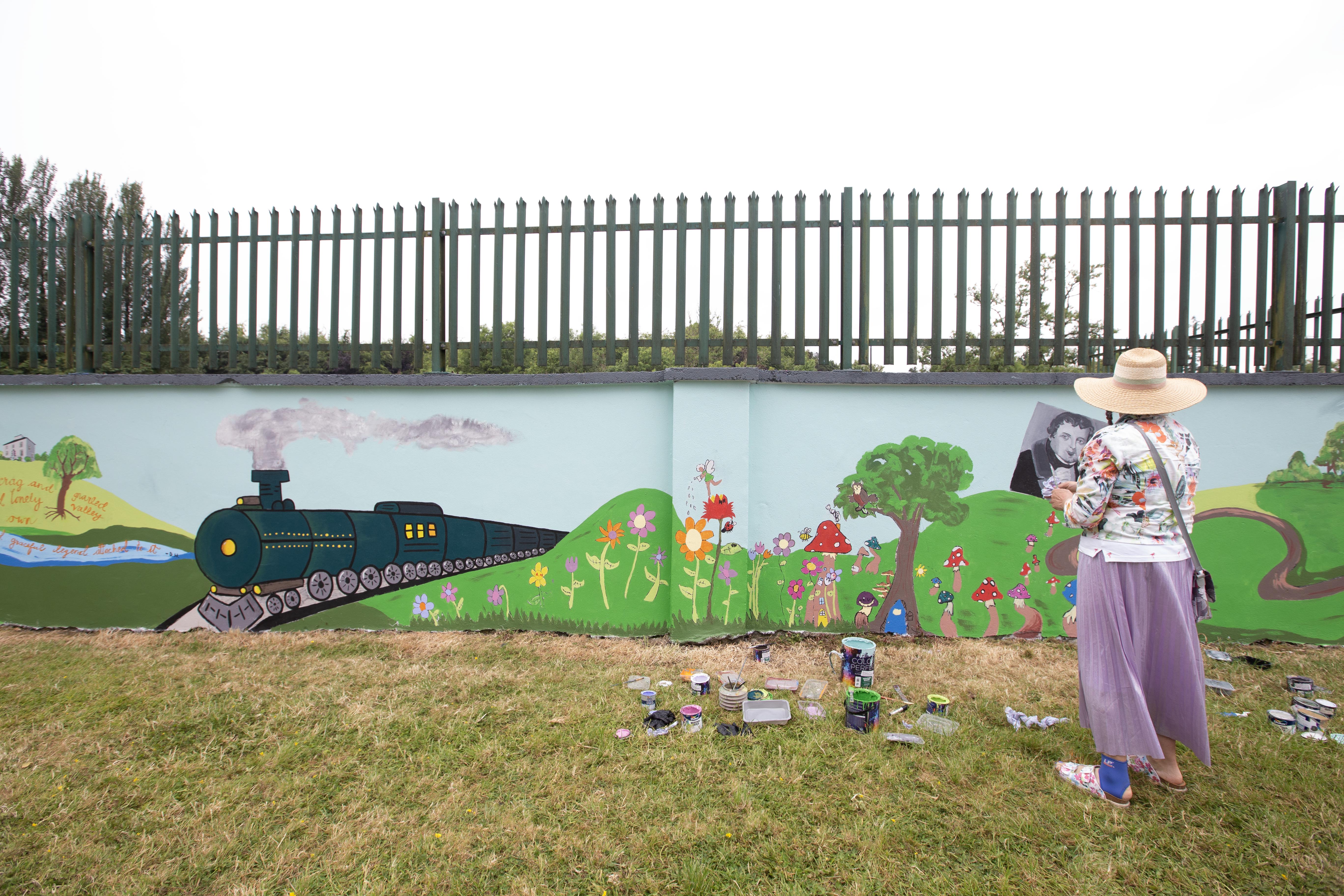 Photo of artist near new painted mural made in collaboration with youth groups